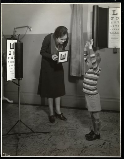 Nurse and a boy patient having an eye test at the New York Association for the Blind, 111 East 59th Street, New York, 1930 by Byron Company